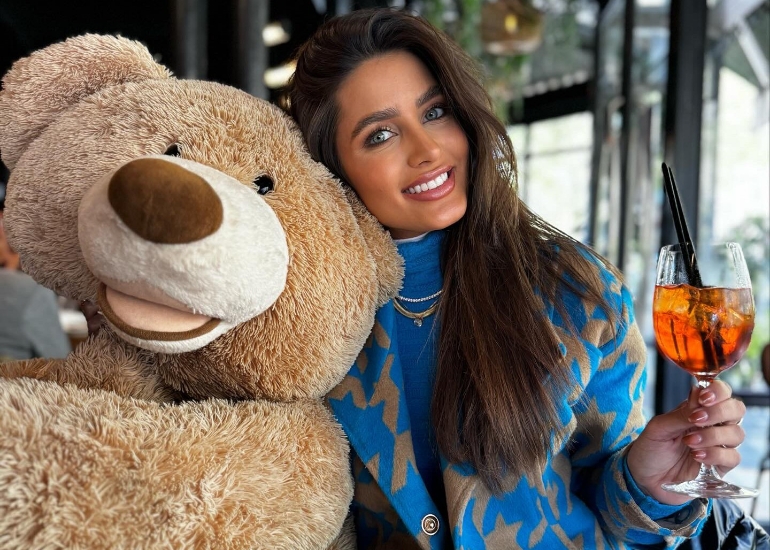 Femme brune tenant un apérol spritz dans sa main droite et un ours en peluche dans sa main gauche au restaurant le Choupinet à Paris