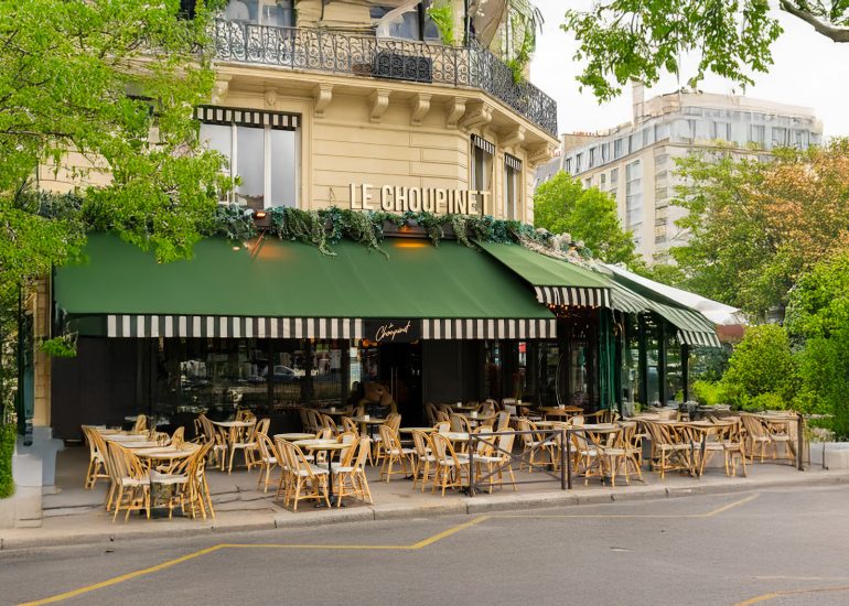 Terrasse extérieure du restaurant parisien Le Choupinet avec une enseigne verte et fleurie, des mobiliers de restauration en extérieur : chaises et tables en bois.