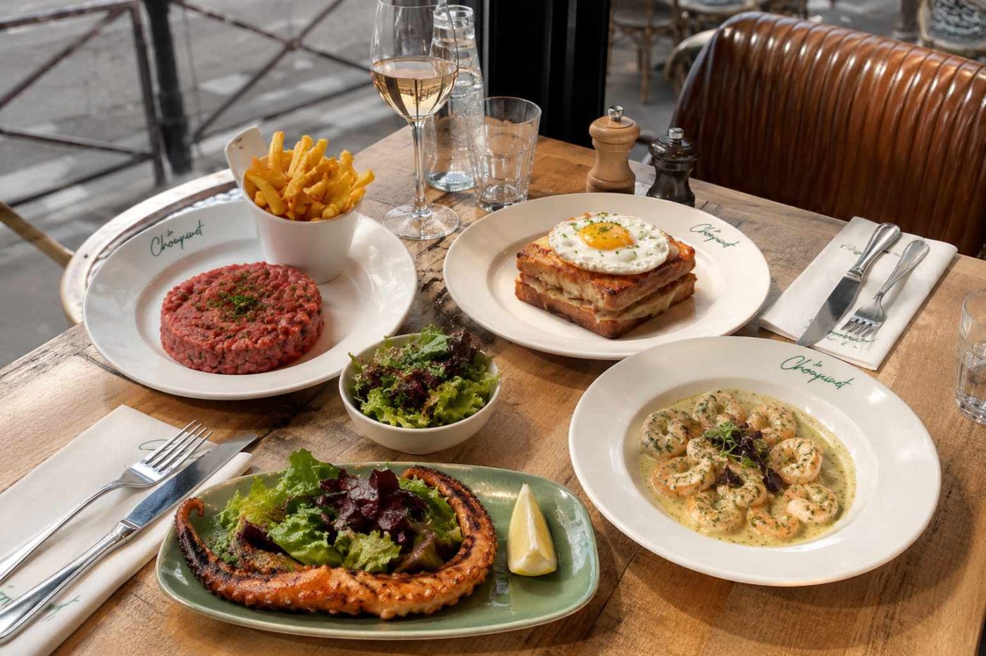 Table du restaurant Le Choupinet avec un steak tartare, un Croque Choupinet, du poulpe grillé et des gambas, présentés dans une ambiance de brasserie parisienne en terrasse.