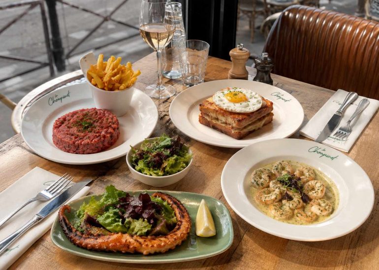 Table du restaurant Le Choupinet avec un steak tartare, un Croque Choupinet, du poulpe grillé et des gambas, présentés dans une ambiance de brasserie parisienne en terrasse.